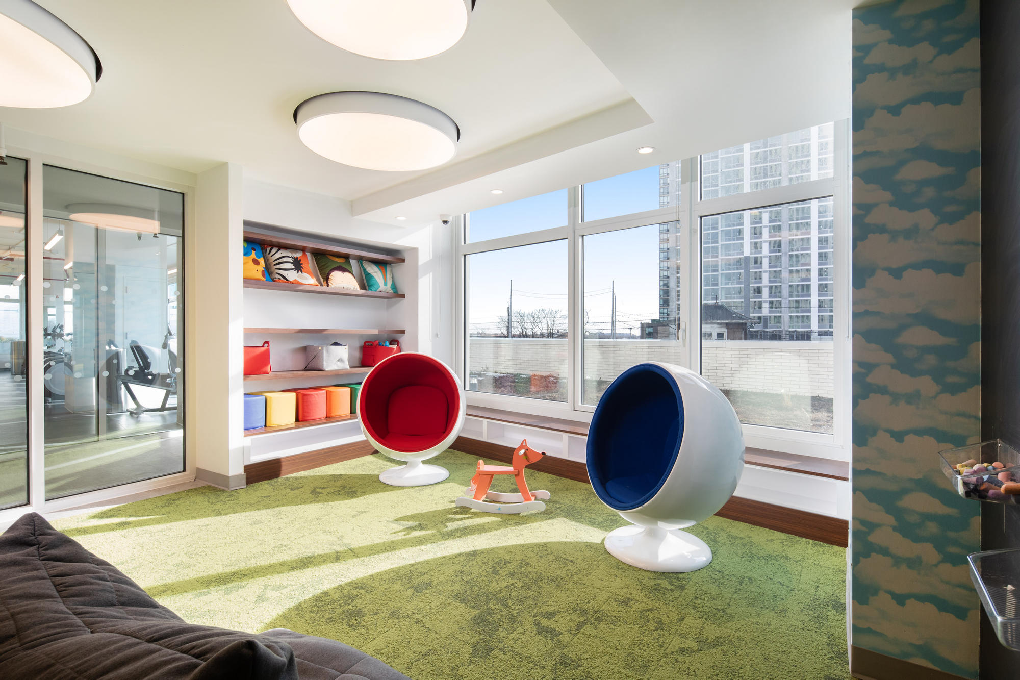Bright children's playroom with fun seating, green carpeted floor, shelves with bins and cute pillows